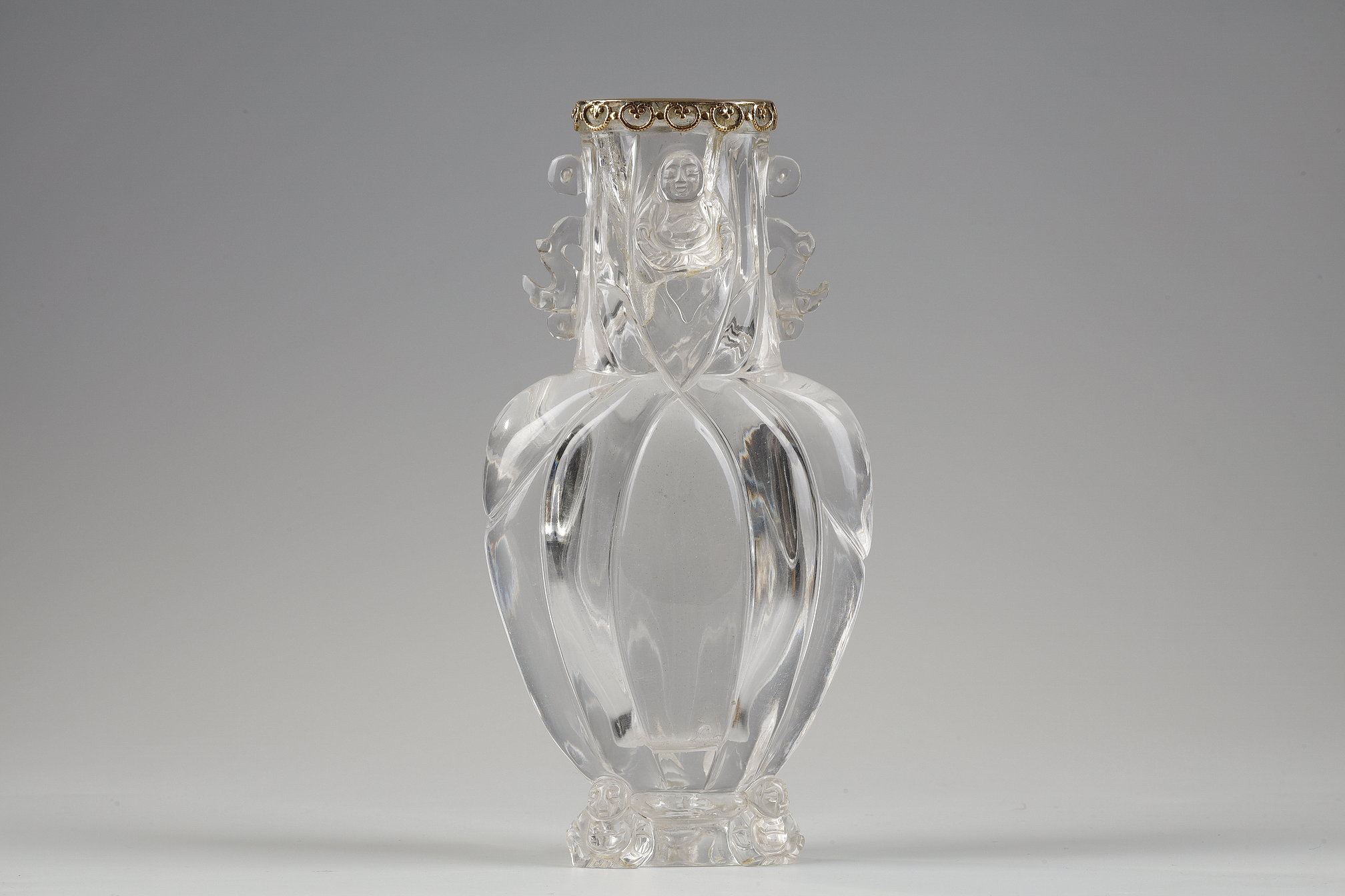 Carved rock crystal vase, the polylobed body, budai leaning against the foot and collar, the handles in the shape of stylized dragons. China around 1900 
The collar rimmed with gold metal in the shape of a lingzhi       H 13.6cm